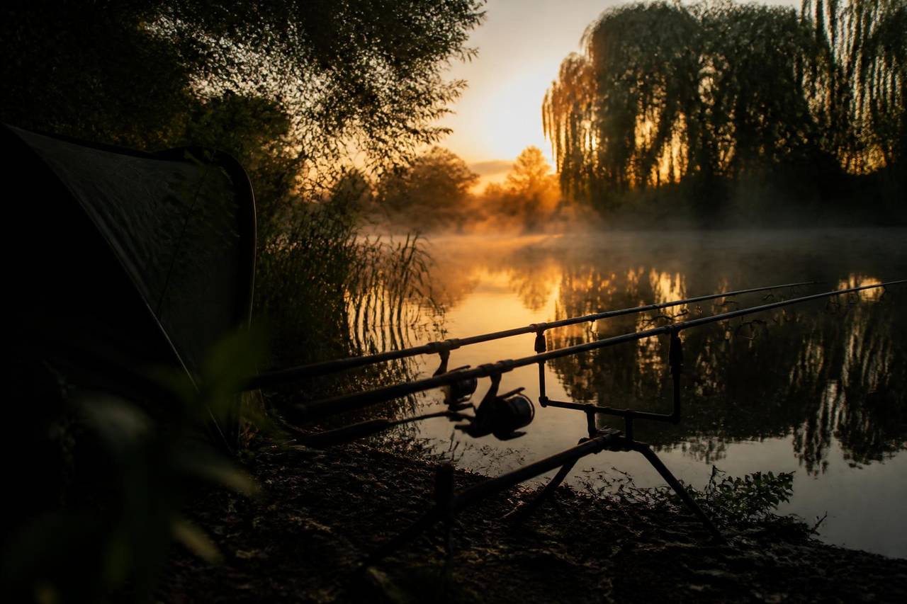 English carp lake at first light with rods on a pod and a bivvy on the bank